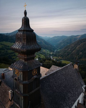Foto de Un disparo vertical de un dron de la torre del reloj de una iglesia en un pequeño pueblo austriaco en las montañas - Imagen libre de derechos