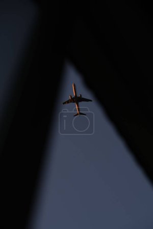 Foto de Un disparo vertical de un avión comercial visto volando en el aire a través de un pequeño hueco - Imagen libre de derechos