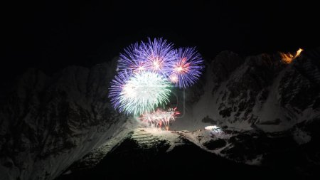 Foto de Un disparo aéreo de fuegos artificiales de colores en la cima de una montaña cubierta de nieve durante la noche - Imagen libre de derechos