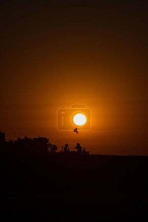 Téléchargez les photos : Une silhouette de personnes assises sur la plage à une heure d'or coucher de soleil - en image libre de droit