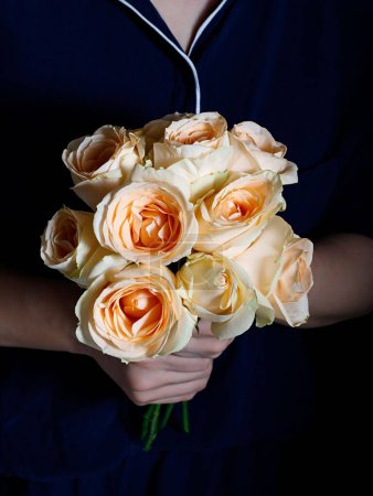 Photo for A vertical shot of a woman holding a bouquet of colorful roses in a studio in a dark background - Royalty Free Image