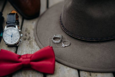 Téléchargez les photos : Gros plan d'un chapeau masculin avec des bagues de fiançailles sur la jante, une montre et un nœud papillon rouge - en image libre de droit