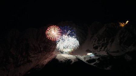 Foto de Un disparo aéreo de fuegos artificiales de colores en la cima de una montaña cubierta de nieve durante la noche - Imagen libre de derechos