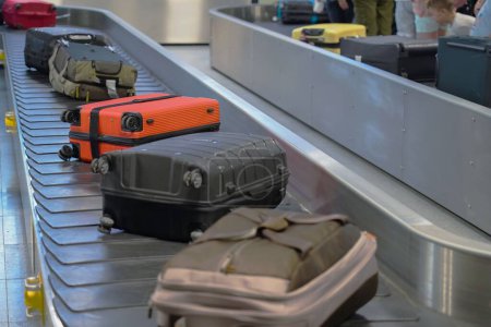Téléchargez les photos : Les valises sur un carrousel à bagages dans un aéroport avec des invités en arrière-plan - en image libre de droit