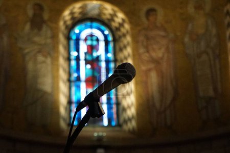 Foto de Un primer plano de un micrófono en una iglesia con un fondo borroso de una ventana colorida - Imagen libre de derechos