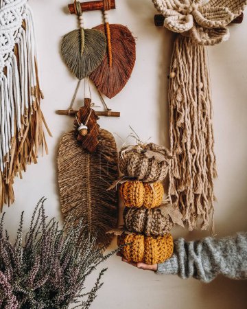 Photo for A woman holding macrame pumpkins with macrame feathers hanging on a white wall in the background - Royalty Free Image