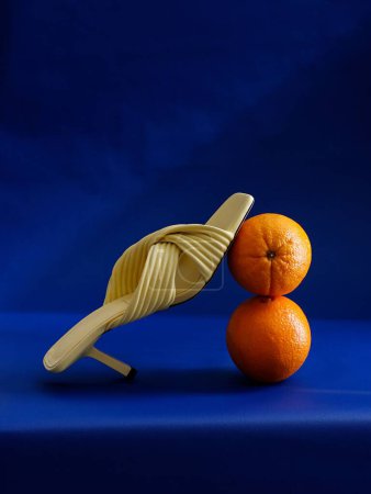 Foto de Sandalia de tacón alto color crema con 2 naranjas sobre fondo azul - plano vertical - Imagen libre de derechos