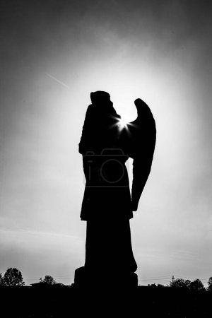 Téléchargez les photos : Un plan en niveaux de gris de la silhouette d'une statue d'ange avec des ailes sous un ciel nuageux au coucher du soleil - en image libre de droit