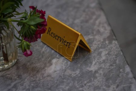 Téléchargez les photos : Un gros plan d'un panneau "Réservé" doré sur une table avec des fleurs dans un restaurant - en image libre de droit