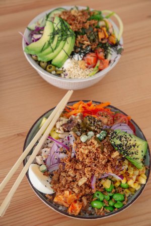 Photo for A vertical top view of poke bowls with vegetables on a wooden table - Royalty Free Image