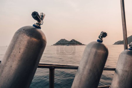 Téléchargez les photos : Les bouteilles de réservoir pour la plongée sous-marine avec une mer et une île en arrière-plan - en image libre de droit