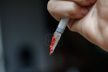 Téléchargez les photos : Une main dans un gant en plastique vert tenant un scalpel couvert de sang - en image libre de droit