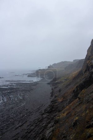 Téléchargez les photos : Une falaise rocheuse au bord de la mer avec un ciel nuageux brumeux à l'horizon, plan vertical - en image libre de droit