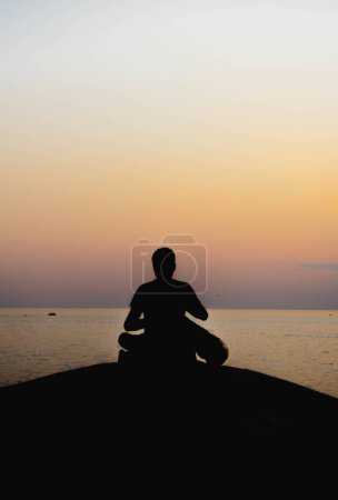 Téléchargez les photos : Plan vertical d'une silhouette d'une personne méditant sur le bord de mer au coucher du soleil - en image libre de droit