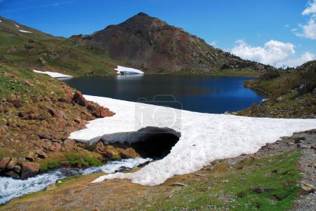 Téléchargez les photos : Une rivière coulant sous un arc de glace avec un fond de lac entre les montagnes - en image libre de droit