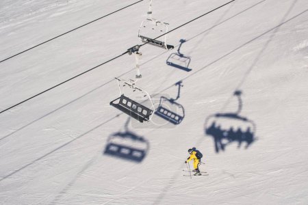 Photo for An aerial view of a person skiing on the slope of the mountain under the chair lift - Royalty Free Image