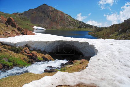 Téléchargez les photos : Une rivière coulant sous un arc de glace avec un fond de lac entre les montagnes - en image libre de droit