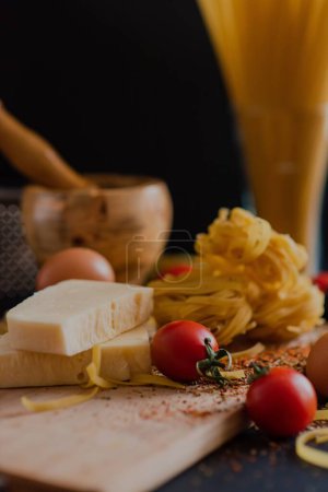 Photo for A view of pasta on a wooden board sprinkled with spice, tomatoes, cheese, two eggs and a grinding bowl - Royalty Free Image