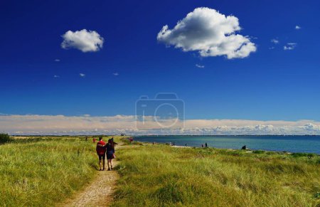 Photo for An image of a road surrounded with grass and people walking on it, the Baltic Sea on the right and a beautiful sky in Germany - Royalty Free Image