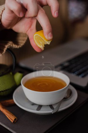 Photo for A vertical shot of a female hand squeezing lemon into her tea in a cafe - Royalty Free Image