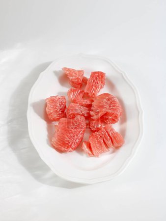Foto de Una toma vertical de un plato de piezas de pomelo rojo sobre una mesa blanca - Imagen libre de derechos