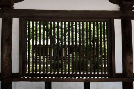 Foto de Tradicional asiático barras de madera en una ventana con vegetación detrás de ella - Imagen libre de derechos
