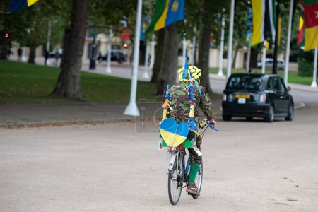 Foto de Escena de una persona vestida de militar montada en bicicleta con una bandera ucraniana en forma de corazón detrás de la bicicleta - Imagen libre de derechos