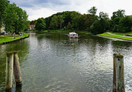 Téléchargez les photos : Une vue panoramique d'un bateau naviguant dans la tranquille rivière Trave entourée d'arbres à feuilles persistantes en Allemagne - en image libre de droit