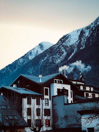 Foto de Edificios de casas de madera bajo montañas nevadas bajo cielo gris nublado, plano vertical - Imagen libre de derechos