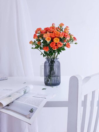 Foto de Un plano vertical de un hermoso ramo de rosas en un jarrón de cristal azul sobre una mesa blanca con una revista - Imagen libre de derechos