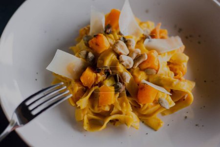 Photo for A closeup of pasta with pumpkin on a white plate with a fork near - Royalty Free Image