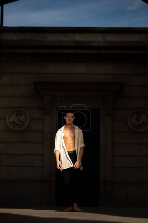 Téléchargez les photos : Un beau jeune homme posant avec une chemise déboutonnée sous le soleil chaud - en image libre de droit