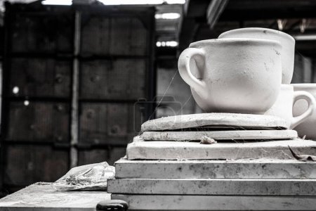 Foto de Una toma a escala de grises de tazas de cerámica hechas a mano en una pila de tablas en el taller - Imagen libre de derechos