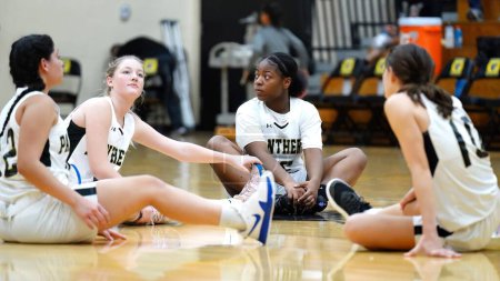 Téléchargez les photos : Une jeune équipe féminine s'étirant sur un terrain intérieur lors d'un match de basket-ball des filles du lycée - en image libre de droit