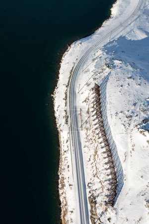 Téléchargez les photos : Vue aérienne verticale d'une route dans le champ blanc enneigé à flanc de colline sur le rivage - en image libre de droit