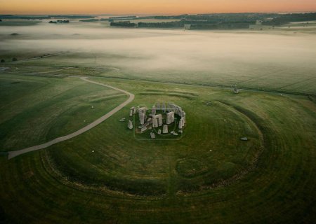 A drone shot of the Stonehenge prehistoric monument in green landscape at dusk in Wiltshire, England