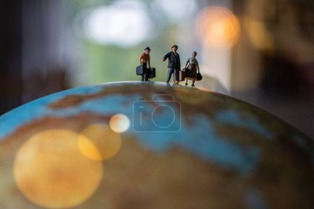 Téléchargez les photos : Un gros plan de personnes miniatures tenant des bagages marchant sur une surface du globe - en image libre de droit