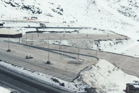 Téléchargez les photos : Vue aérienne d'un parking et d'une seule voiture garée là entourée de collines enneigées - en image libre de droit