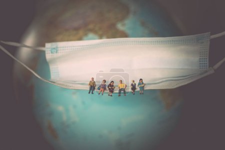 Foto de Un primer plano de personas en miniatura sentadas en una máscara desechable con un globo borroso en el fondo - Imagen libre de derechos