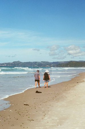 Téléchargez les photos : Une verticale d'un vieux couple marchant au bord de la mer en Nouvelle-Zélande par une journée ensoleillée aux couleurs vintage - en image libre de droit