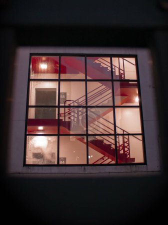 Foto de Una vertical de escaleras rojas, escaleras vistas desde una ventana cuadrada con protectores de ventanas - Imagen libre de derechos