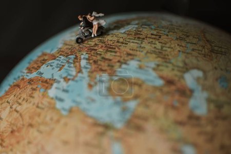 Photo for A closeup of miniature bride and groom on a motorbike on a globe surface - Royalty Free Image