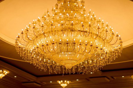 Foto de Una foto de bajo ángulo de una lujosa lámpara de araña colgada en un techo, con muchas bombillas encendidas, decoradas con adornos vidriosos colgantes - Imagen libre de derechos