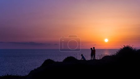 Foto de Las siluetas de los niños en la costa de un mar en una puesta de sol naranja brillante - Imagen libre de derechos