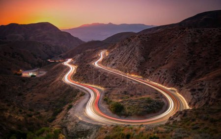 Foto de Un paisaje de carreteras en colinas con senderos de coches de larga exposición durante una hermosa puesta de sol - Imagen libre de derechos