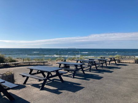 Téléchargez les photos : Tables de pique-nique sur la côte surplombant le magnifique paysage marin par une journée ensoleillée - en image libre de droit