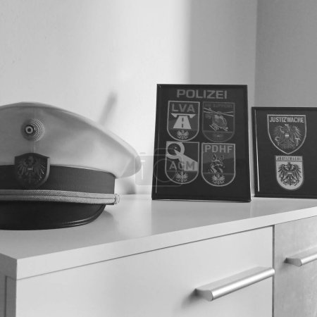 Foto de Un primer plano a escala de grises de una gorra colocada junto a los iconos de la policía alemana en marcos - Imagen libre de derechos