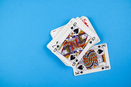 Photo for A closeup of a deck of playing cards with the queen and king of spades facing up on a blue background - Royalty Free Image