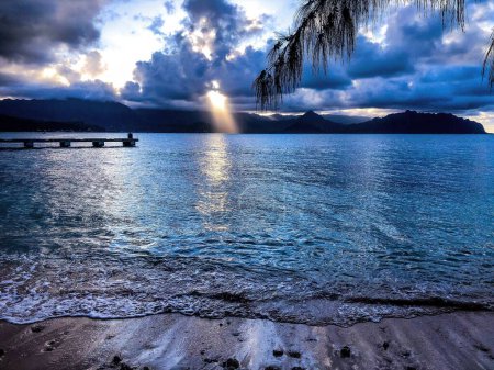 Foto de Un hermoso amanecer tranquilo detrás de las nubes esponjosas sobre la orilla del mar con las colinas en el fondo - Imagen libre de derechos