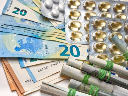 Téléchargez les photos : Un médicament dans un paquet couché sur une pile de billets en euros - en image libre de droit